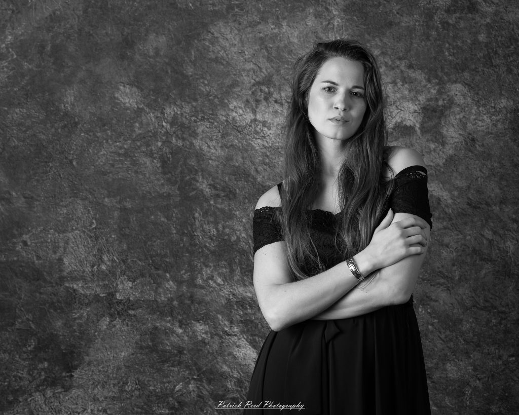 Black-and-white portrait of a woman standing with arms crossed against a textured backdrop.