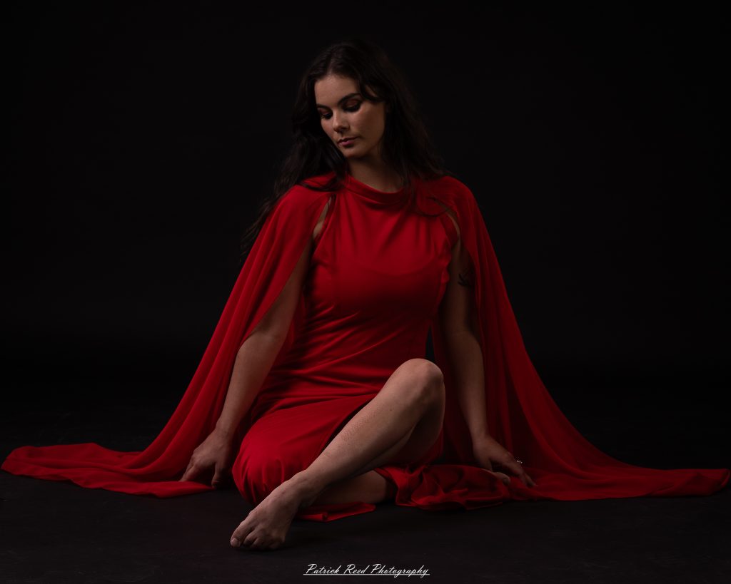 Black and white fine art dance portrait of a dancer in a flowing dress, captured in motion with expressive movement and soft studio lighting against a dark background.