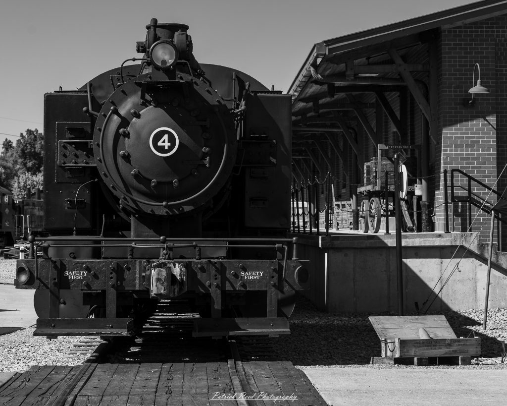 Black-and-white documentary photographs from the Steam Railroading Institute in Ohio, featuring historic steam locomotives, vintage passenger railcars, railroad machinery, restoration workshops, and industrial details preserving America's railroad heritage.