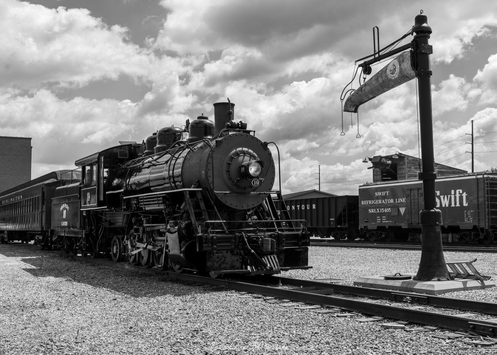 Black-and-white documentary photographs from the Steam Railroading Institute in Ohio, featuring historic steam locomotives, vintage passenger railcars, railroad machinery, restoration workshops, and industrial details preserving America's railroad heritage.