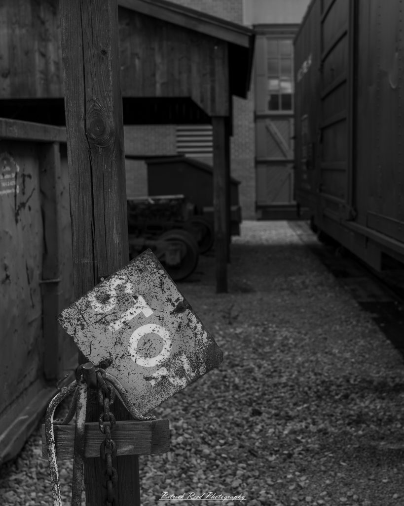 Black-and-white documentary photographs from the Steam Railroading Institute in Ohio, featuring historic steam locomotives, vintage passenger railcars, railroad machinery, restoration workshops, and industrial details preserving America's railroad heritage.