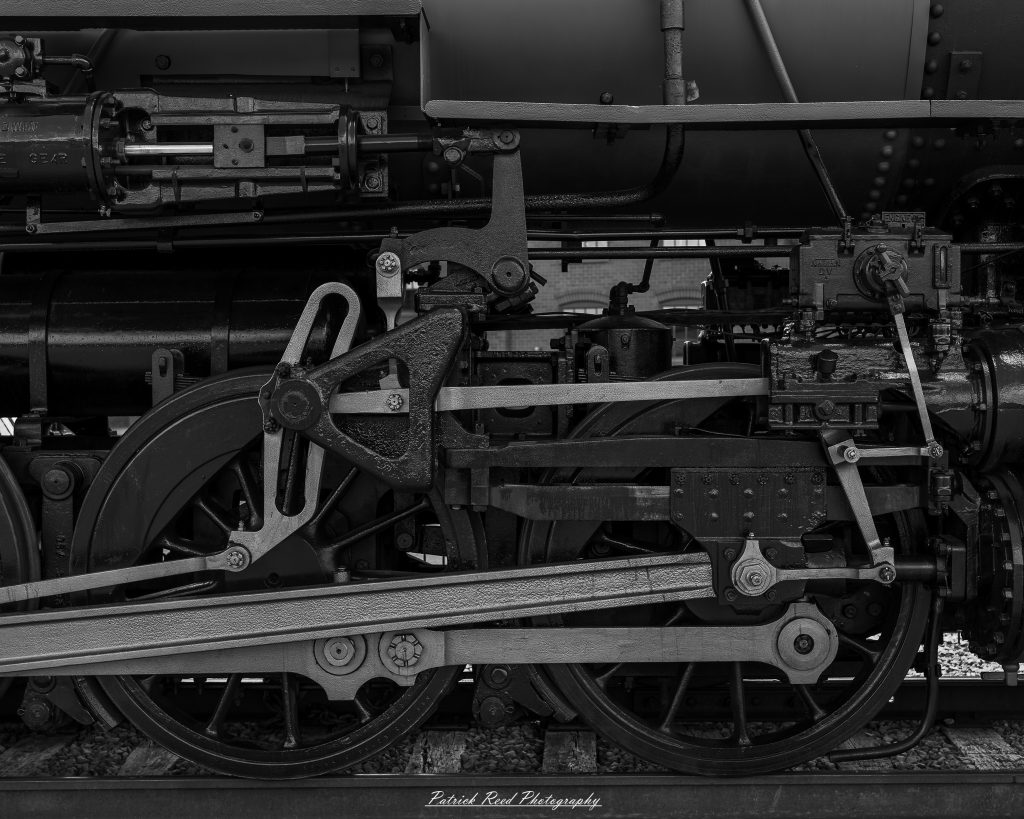 Black-and-white documentary photographs from the Steam Railroading Institute in Ohio, featuring historic steam locomotives, vintage passenger railcars, railroad machinery, restoration workshops, and industrial details preserving America's railroad heritage.