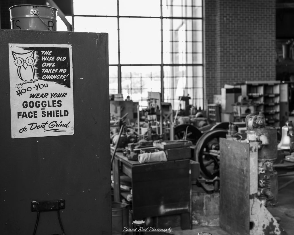 Black-and-white documentary photographs from the Steam Railroading Institute in Ohio, featuring historic steam locomotives, vintage passenger railcars, railroad machinery, restoration workshops, and industrial details preserving America's railroad heritage.