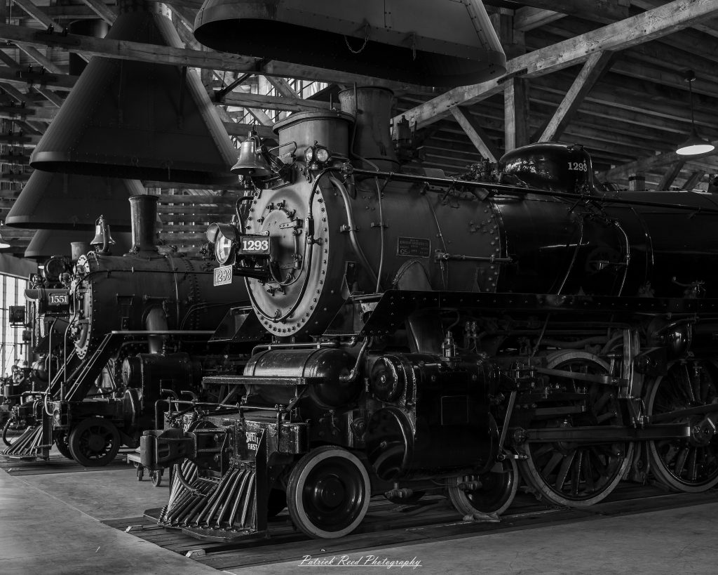 Black-and-white documentary photographs from the Steam Railroading Institute in Ohio, featuring historic steam locomotives, vintage passenger railcars, railroad machinery, restoration workshops, and industrial details preserving America's railroad heritage.