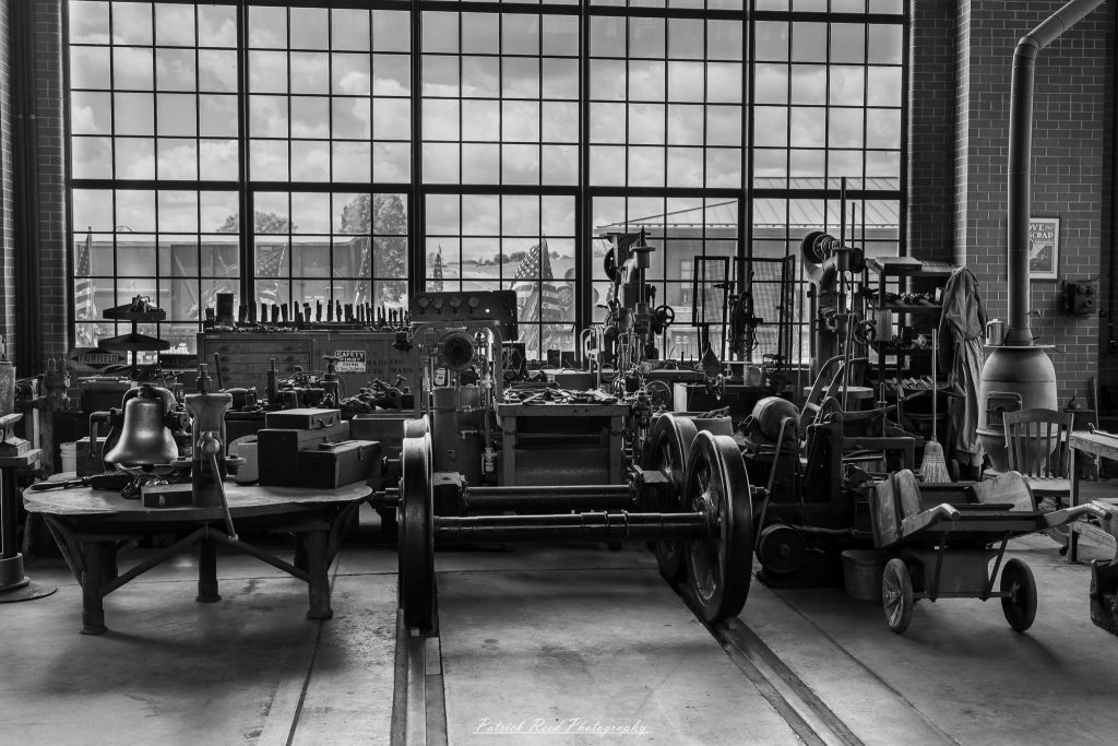 Black-and-white documentary photographs from the Steam Railroading Institute in Ohio, featuring historic steam locomotives, vintage passenger railcars, railroad machinery, restoration workshops, and industrial details preserving America's railroad heritage.