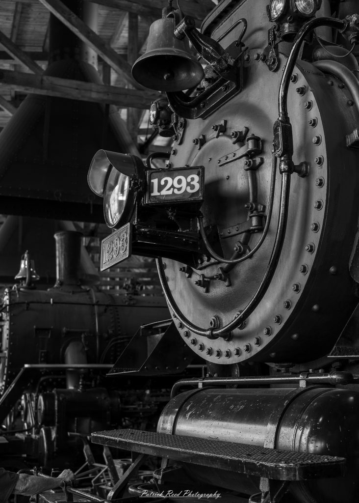 Black-and-white documentary photographs from the Steam Railroading Institute in Ohio, featuring historic steam locomotives, vintage passenger railcars, railroad machinery, restoration workshops, and industrial details preserving America's railroad heritage.