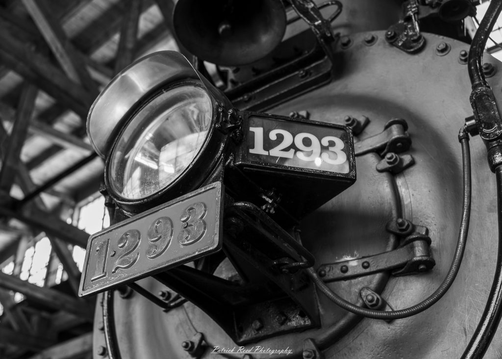 Black-and-white documentary photographs from the Steam Railroading Institute in Ohio, featuring historic steam locomotives, vintage passenger railcars, railroad machinery, restoration workshops, and industrial details preserving America's railroad heritage.