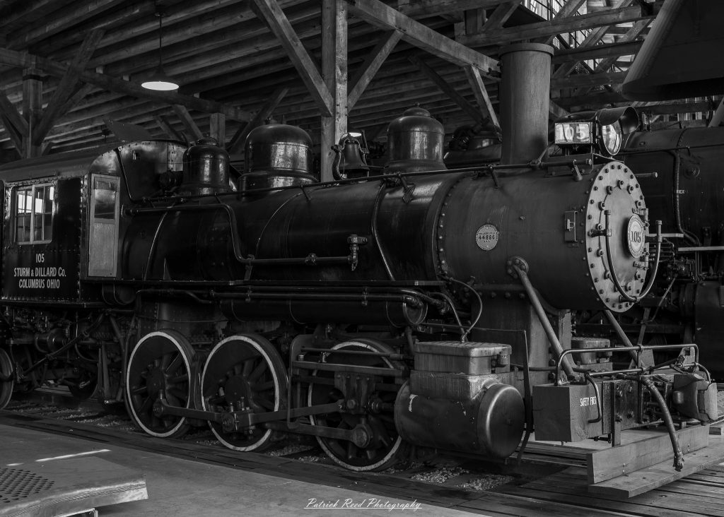 Black-and-white documentary photographs from the Steam Railroading Institute in Ohio, featuring historic steam locomotives, vintage passenger railcars, railroad machinery, restoration workshops, and industrial details preserving America's railroad heritage.