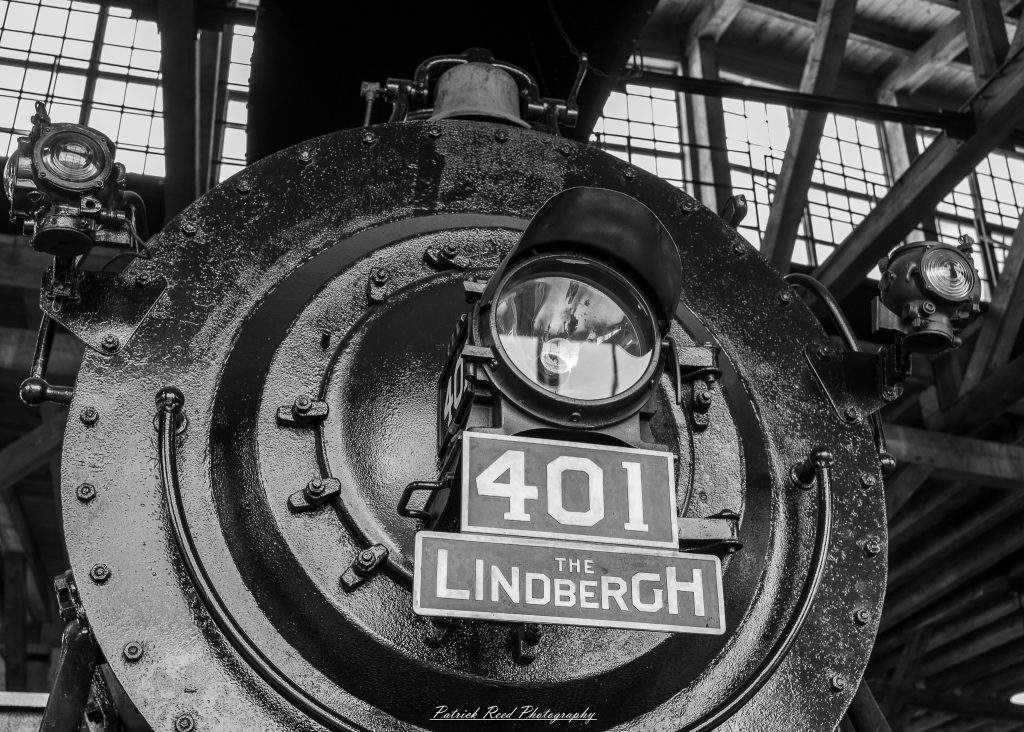 Black-and-white documentary photographs from the Steam Railroading Institute in Ohio, featuring historic steam locomotives, vintage passenger railcars, railroad machinery, restoration workshops, and industrial details preserving America's railroad heritage.