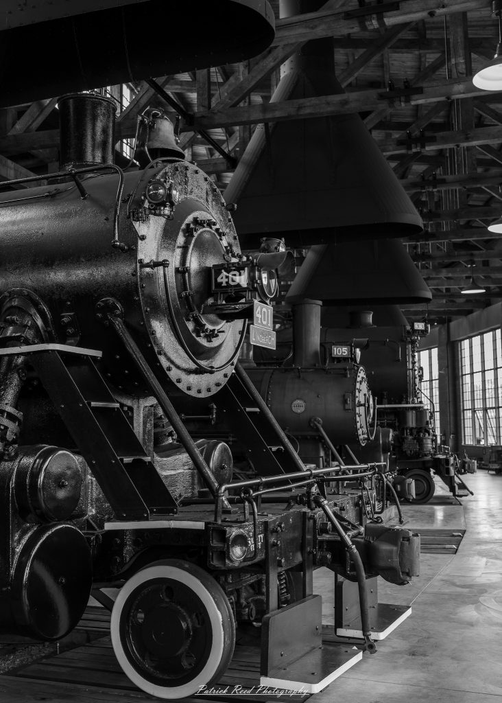 Black-and-white documentary photographs from the Steam Railroading Institute in Ohio, featuring historic steam locomotives, vintage passenger railcars, railroad machinery, restoration workshops, and industrial details preserving America's railroad heritage.