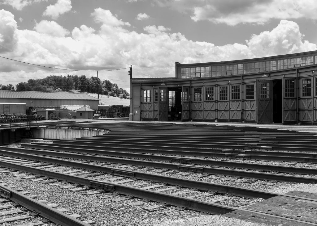Black-and-white documentary photographs from the Steam Railroading Institute in Ohio, featuring historic steam locomotives, vintage passenger railcars, railroad machinery, restoration workshops, and industrial details preserving America's railroad heritage.