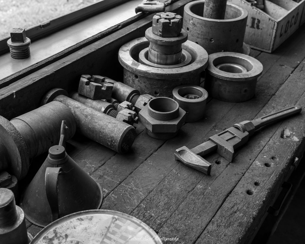 Black-and-white documentary photographs from the Steam Railroading Institute in Ohio, featuring historic steam locomotives, vintage passenger railcars, railroad machinery, restoration workshops, and industrial details preserving America's railroad heritage.