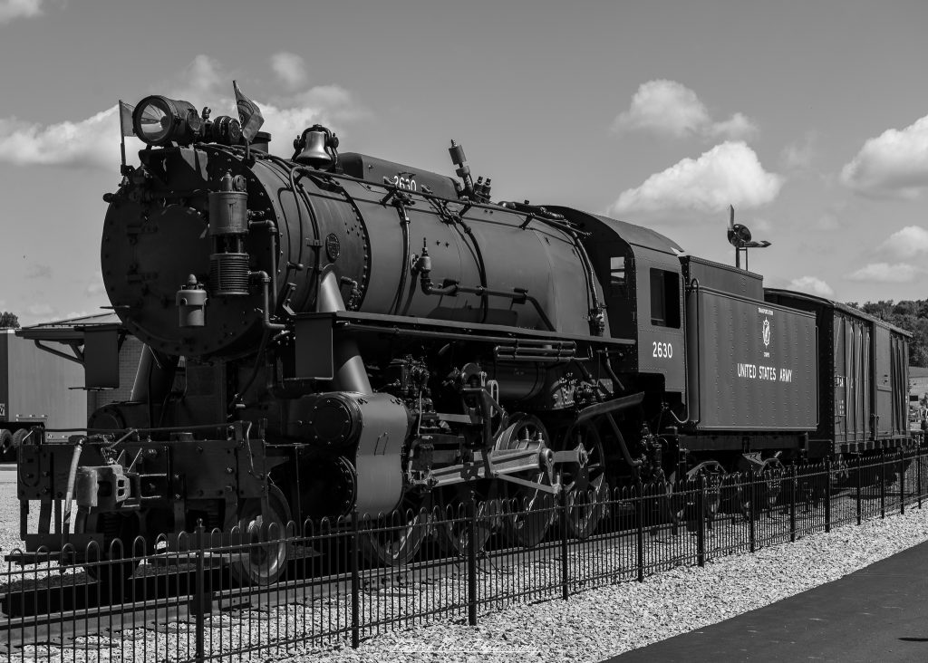 Black-and-white documentary photographs from the Steam Railroading Institute in Ohio, featuring historic steam locomotives, vintage passenger railcars, railroad machinery, restoration workshops, and industrial details preserving America's railroad heritage.