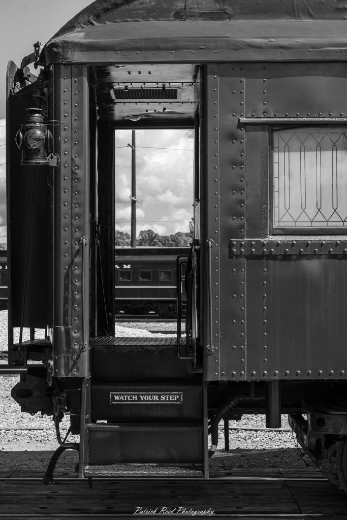 Black-and-white documentary photographs from the Steam Railroading Institute in Ohio, featuring historic steam locomotives, vintage passenger railcars, railroad machinery, restoration workshops, and industrial details preserving America's railroad heritage.