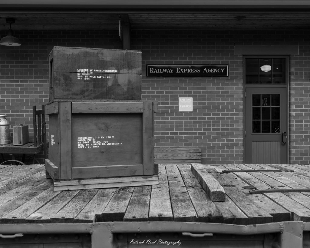 Black-and-white documentary photographs from the Steam Railroading Institute in Ohio, featuring historic steam locomotives, vintage passenger railcars, railroad machinery, restoration workshops, and industrial details preserving America's railroad heritage.
