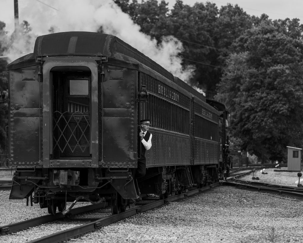 Black-and-white documentary photographs from the Steam Railroading Institute in Ohio, featuring historic steam locomotives, vintage passenger railcars, railroad machinery, restoration workshops, and industrial details preserving America's railroad heritage.
