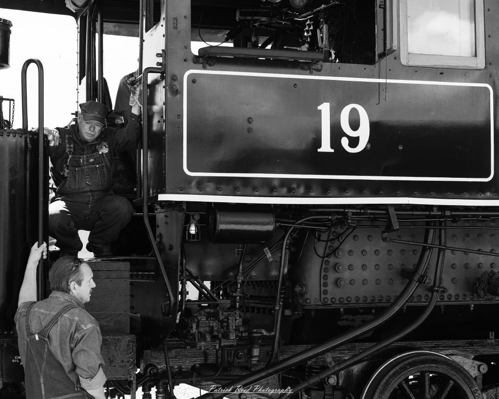 Black-and-white documentary photographs from the Steam Railroading Institute in Ohio, featuring historic steam locomotives, vintage passenger railcars, railroad machinery, restoration workshops, and industrial details preserving America's railroad heritage.