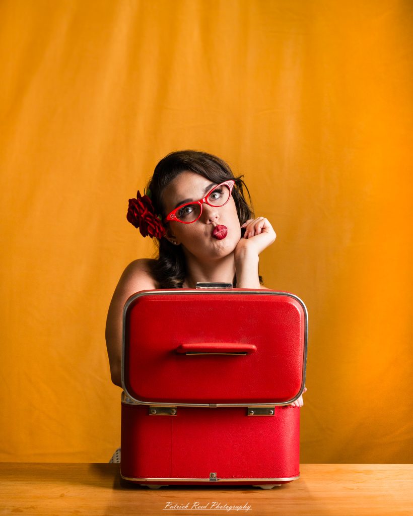 Vintage pin-up portrait photography featuring a model in 1950s-inspired fashion with retro dresses, cat-eye glasses, classic hairstyles, vintage props, and studio lighting. Rockabilly and mid-century glamour portraits created in a professional photography studio.