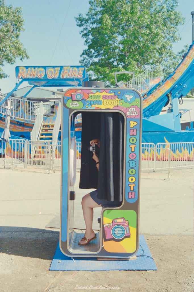 Colorful “Snap Crazy Photo Booth” at an outdoor fair with “Ring of Fire” signs and people waiting.