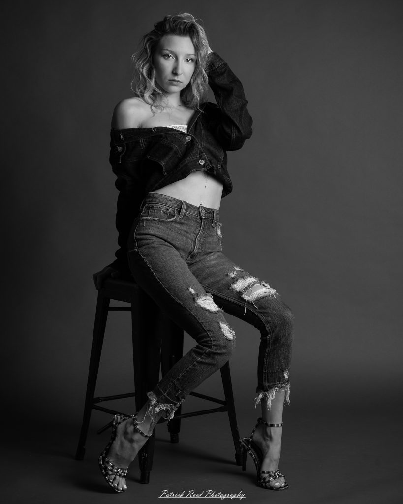 Black-and-white studio portrait series contact sheet featuring a female subject in moody, high-contrast chiaroscuro lighting, showcasing both a fitted black dress with mesh sleeves and a dark denim jacket outfit.