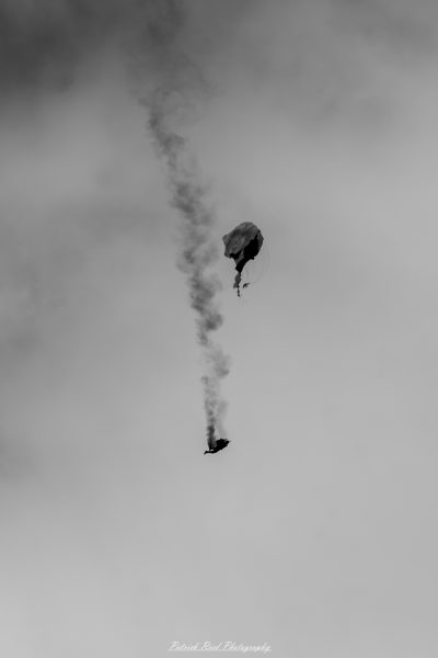 "A parachutist performing a cutaway maneuver during a skydive, captured in mid-air against a clear blue sky. The scene shows the skydiver releasing their main parachute after experiencing a malfunction, with the parachute gracefully billowing away from them. The parachutist is in free fall, wearing a jumpsuit and helmet, with their secondary parachute deployed above them, creating a dramatic contrast of colors against the sky. The excitement and precision of the maneuver illustrate the skill and training required for safe skydiving, showcasing the adrenaline-filled world of parachuting."