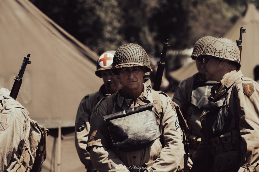 A group of World War II reenactors in period-accurate uniforms—American, German, and French Resistance—on a sandy shore during the D-Day Conneaut 2025 reenactment at Conneaut Township Park, Ohio.