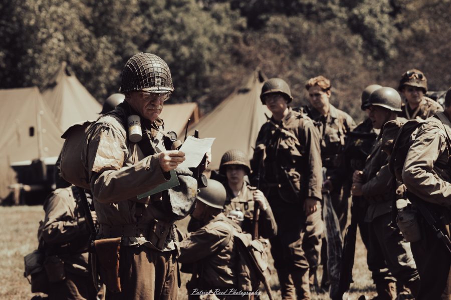 A group of World War II reenactors in period-accurate uniforms—American, German, and French Resistance—on a sandy shore during the D-Day Conneaut 2025 reenactment at Conneaut Township Park, Ohio.