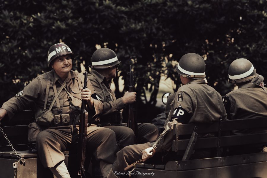 A group of World War II reenactors in period-accurate uniforms—American, German, and French Resistance—on a sandy shore during the D-Day Conneaut 2025 reenactment at Conneaut Township Park, Ohio.