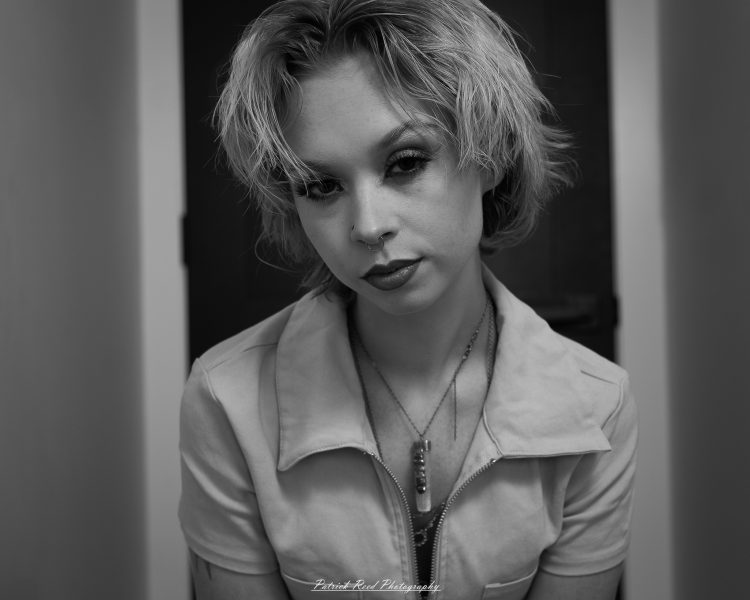 Black-and-white close-up portrait of a person with blonde hair, nose ring, and dark eyes.