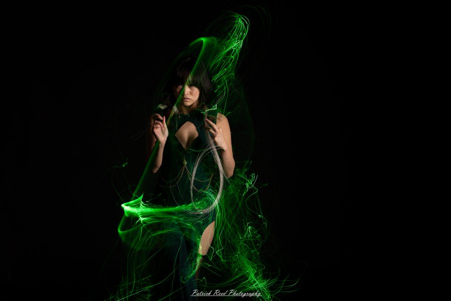 Studio portrait of a woman in a dark dress surrounded by fine green light trails against a black background.