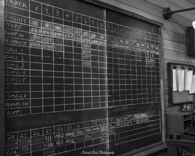Chalkboard tally of steam locomotive engines and track numbers inside a railroad workshop.
