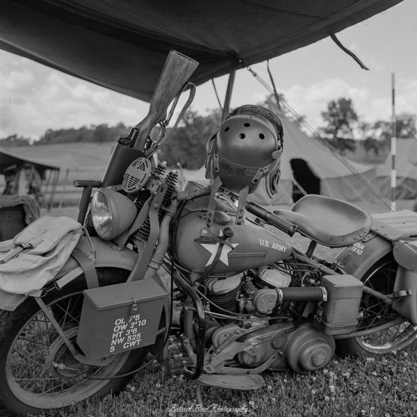 U.S. Army motorcycle with helmet and sidecar under a tent at an outdoor reenactment event.