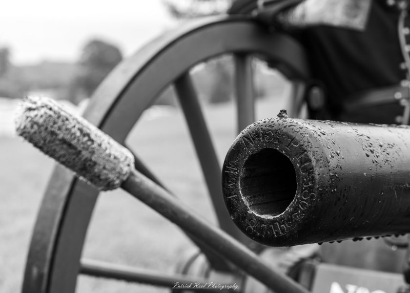Close-up of a vintage Civil War cannon barrel and wheel at an outdoor reenactment.