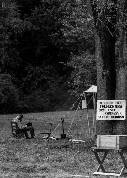 Civil War reenactment campsite with a seated soldier and a banner reading “FREEDOM FOR COLORED MEN!”