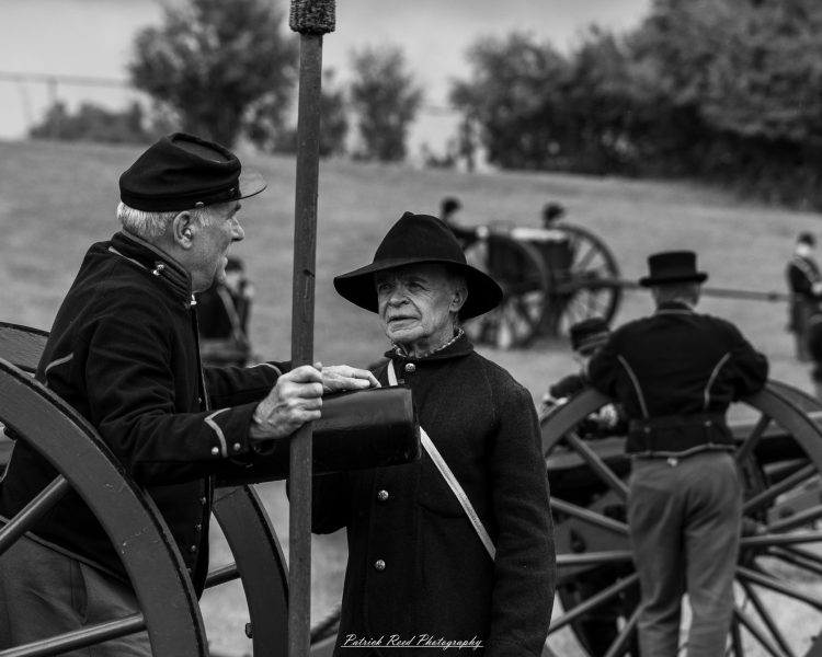 Civil War reenactors in period uniforms stand beside a horse-drawn wagon at an outdoor event.