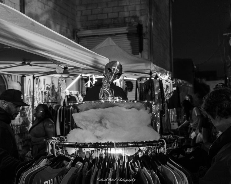 A skull display rises above a circular clothing rack at Eastern Market After Dark, photographed in black and white.