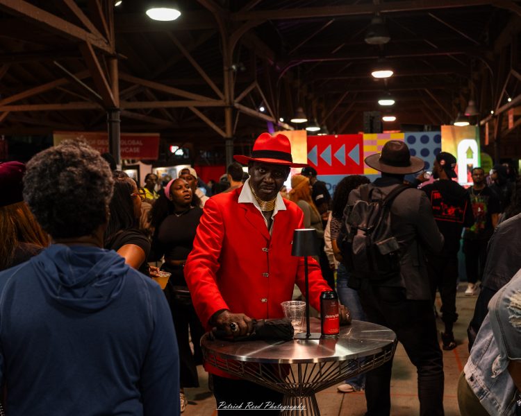 Crowd at a night market as a person raises an arm near the storefront entrance.
