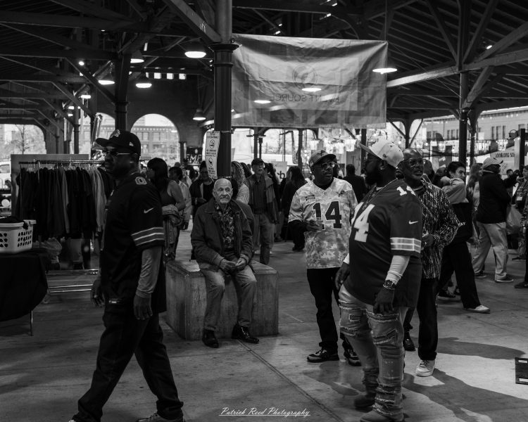 People mingle at night under a covered market pavilion, with event banners hanging overhead.