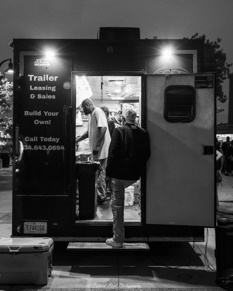 Workers gather inside a lit trailer outside the “Trailer Leasing & Sales” service truck at night.
