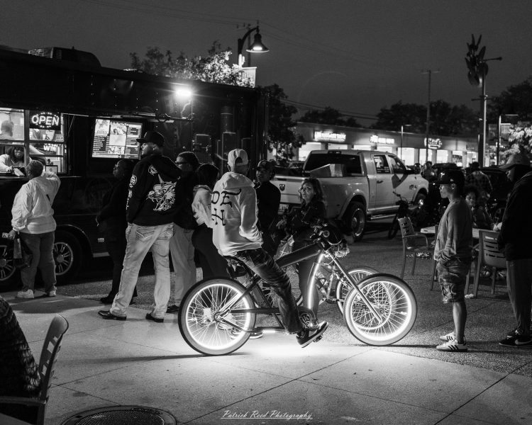 Crowd gathers outside a food truck at night, with an illuminated “OPEN” sign and street lights.